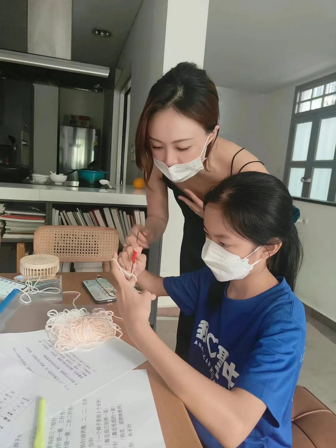 老师在学员身旁，指导学员用钩针和毛线练习钩织