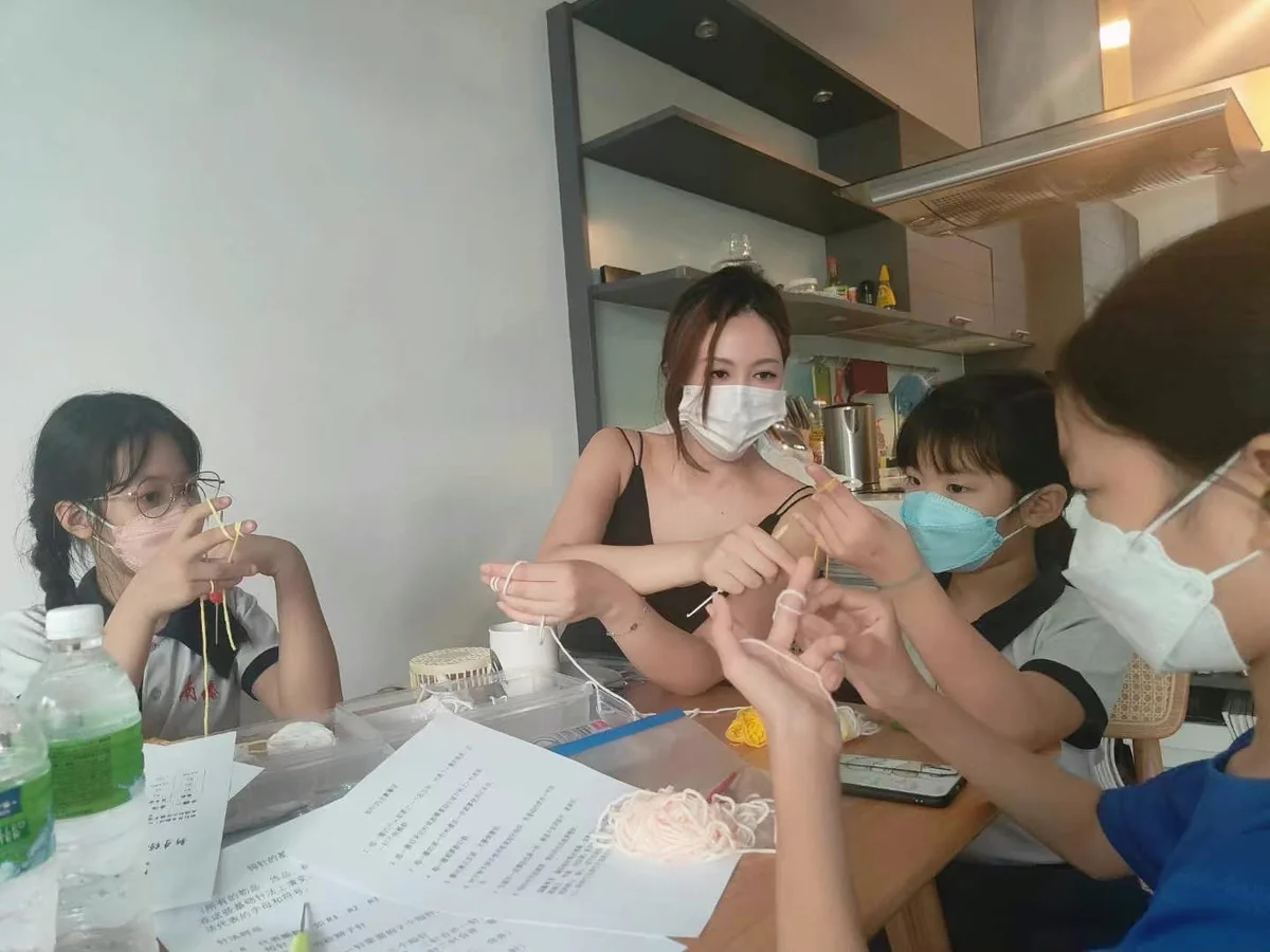 老师指导围坐桌边的小组学员练习拿线及使用钩针